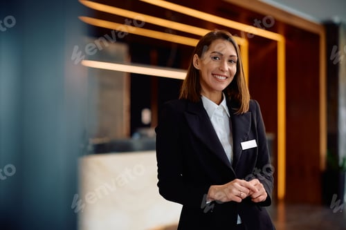 Preview: Happy female concierge in hotel hallway looking at camera.