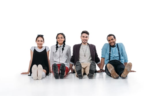 Preview: smiling multiethnic friends sitting on the floor and looking at camera