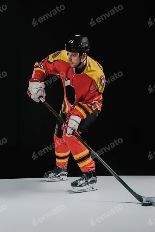 Preview: full length view of professional sportsman playing hockey and looking away on black