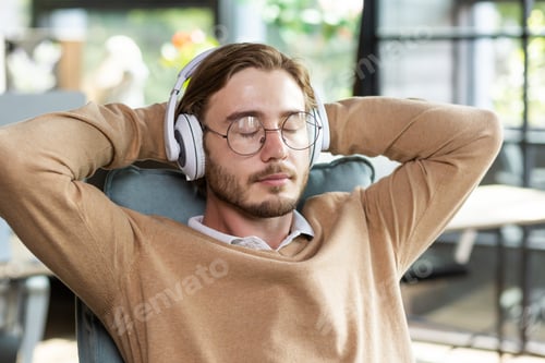Preview: Portrait of a tired office worker in headphones resting at the workplace in a chair, arms crossed