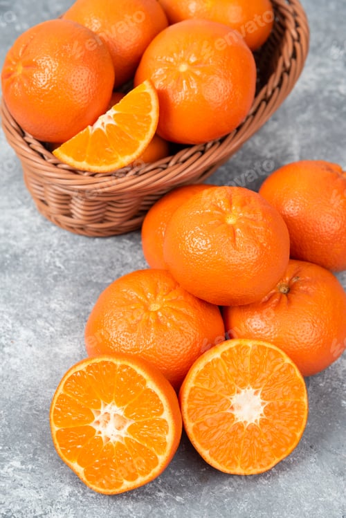 Preview: Whole and slice juicy fresh orange fruits in a wicker basket placed on a stone background