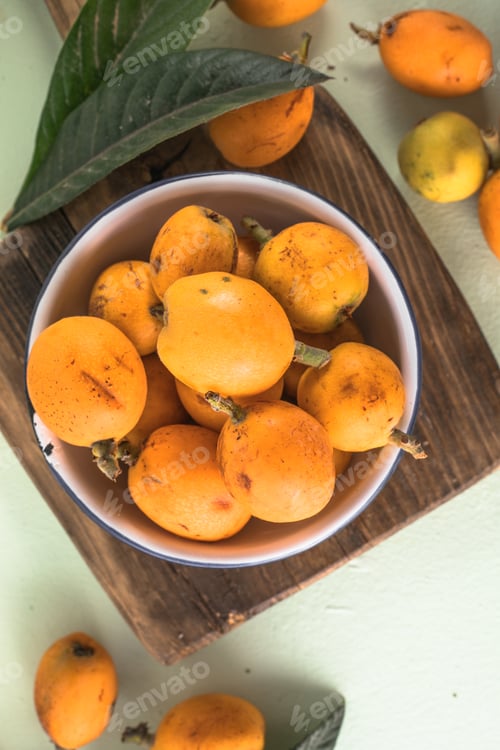 Preview: Ripe medlar fruit , Eriobotrya japonica, and green medlar leaves on wooden table. Top view