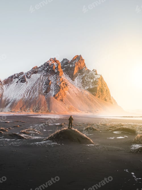 Preview: Person standing on a hill with a stunning mountain landscape at sunrise in Iceland.