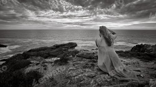 Preview: Grayscale of a blonde woman on a cliffside photographing the ocean