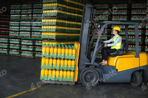 Preview: Forklift operator wearing helmet, hi-vis vest is lifting pallet of orange juice crates in warehouse