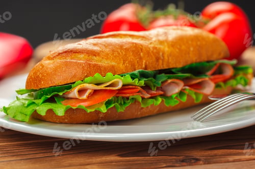 Preview: Fresh sandwich with lettuce, ham, and tomatoes on a plate at a kitchen table