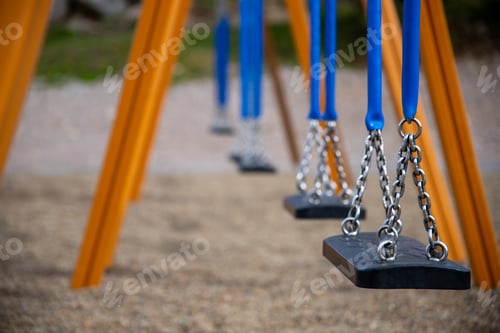 Preview: Soft focus of an empty swing set at a park with yellow and blue paint