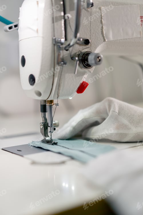 Preview: close up professional dry cleaner young girl hems a patch on a sweater with a sewing machine