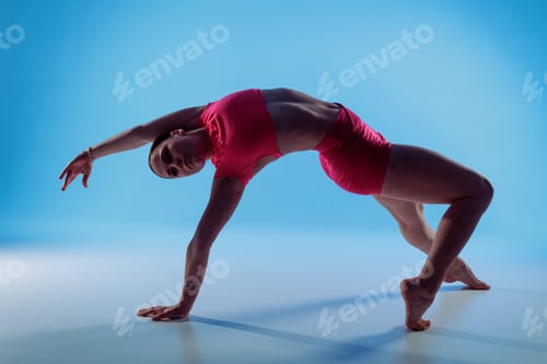Preview: Woman in wild thing yoga backbend pose for mobility and strength on blue studio background
