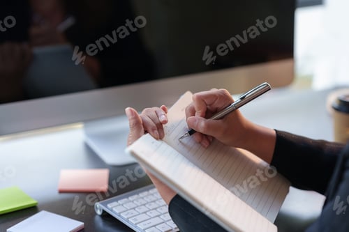 Preview: Close-up of a woman intently writing and taking notes in a notebook in the office.