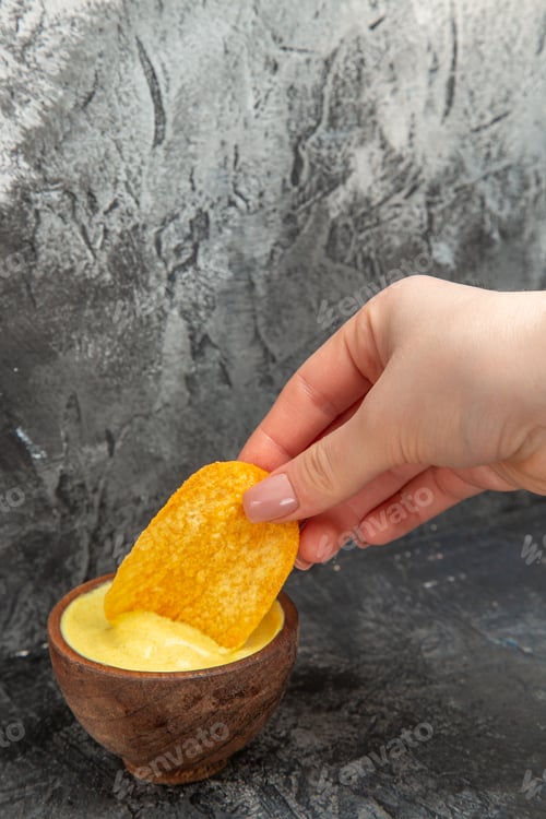 Preview: Hand holding potato chip in a small mayonnaise bowl on gray background