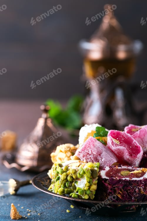 Preview: Bowl with various pieces of turkish delight lokum and black tea with mint on a dark background