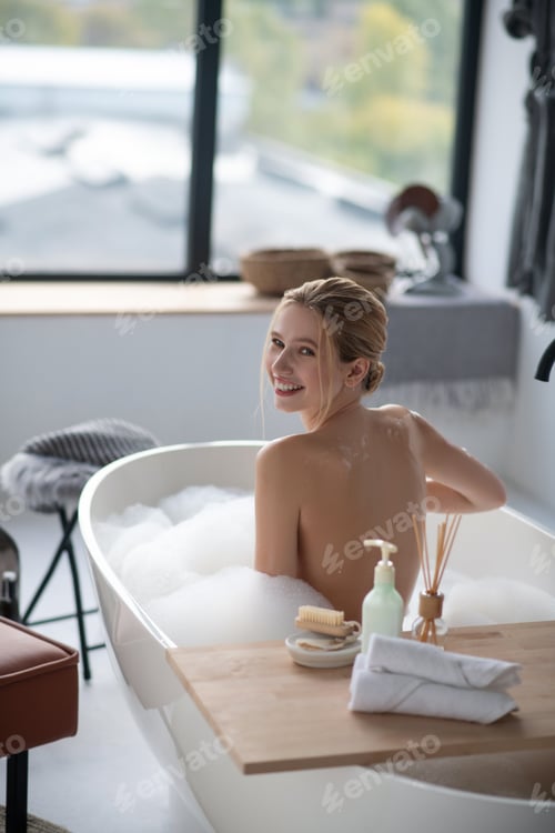 Preview: Woman smiling while enjoying foamy bath in the morning