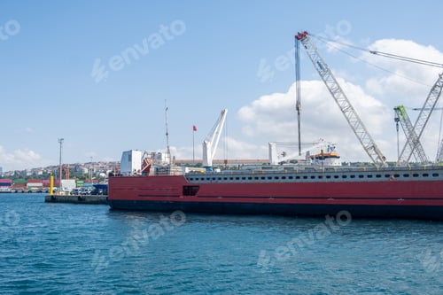 Preview: Large cargo ship docked at the port during a bright sunny day with clear skies and cranes in the