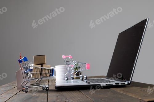 Preview: Composition of shopping carts with boxes and laptop on gray background