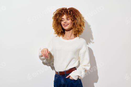 Preview: Smiling young woman with curly hair in a cozy white sweater standing against a plain background