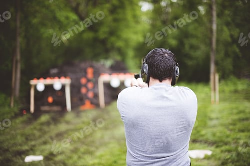 Preview: Shallow focus shot from behind of a male shooting a gun at a gun range