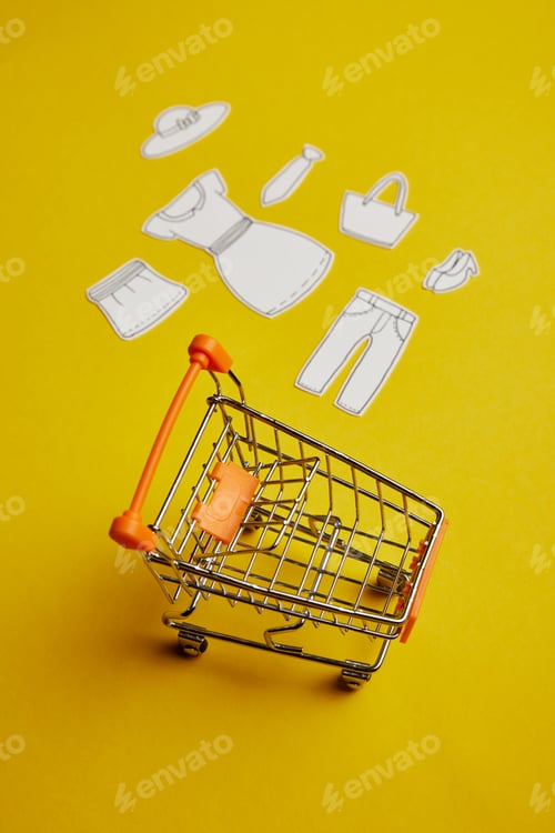 Preview: close up view of little shopping cart and clothes made of paper on yellow background