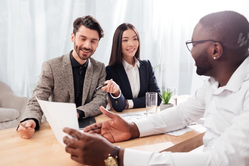 Preview: Happy multinational businessmen and businesswoman sitting at the table discussing documents