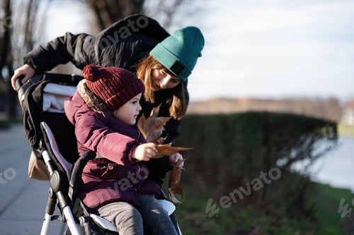 Preview: Young woman in city park with baby stroller. Warm autumn weather for outdoor activity.