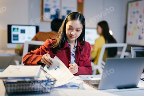 Preview: Asian businesswoman analyzing financial charts and graphs while working on a laptop computer in a mo