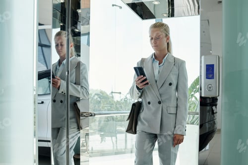 Preview: Young modern businesswoman in grey formalwear texting in mobile phone