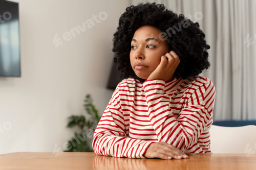 Preview: Sad curly African American woman wearing casual clothes sitting at desk in living room, copy space