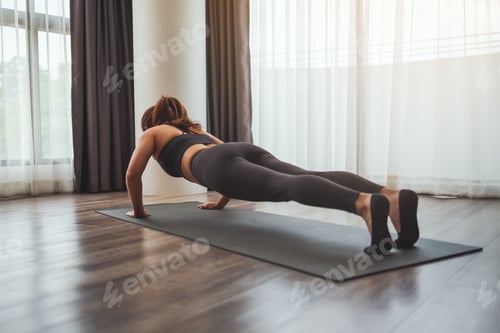 Preview: Rear view image of a young woman doing push up on training mat at home