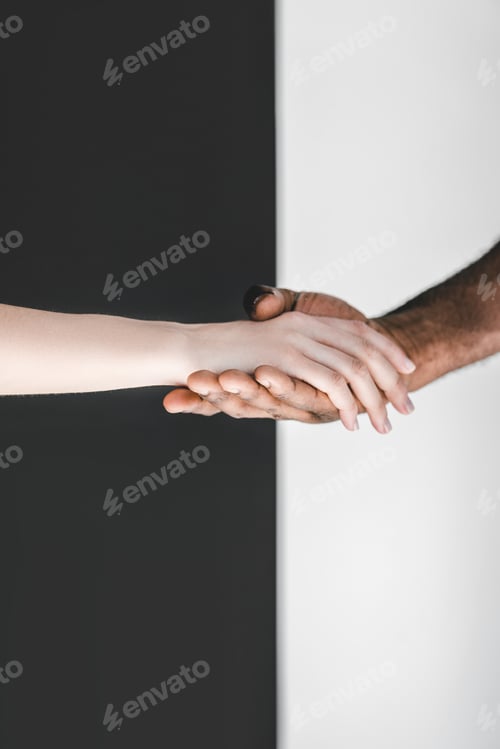 Preview: cropped image of multicultural couple holding hands near black and white wall