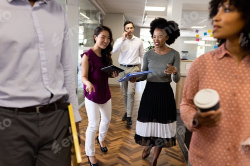 Preview: Diverse happy female and male businesspeople with coffee and documents walking in office