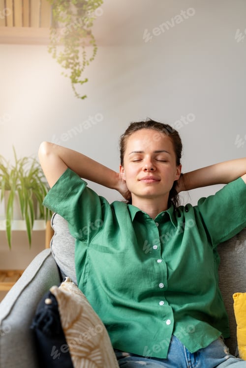 Preview: Portrait of serene woman with hands behind head and closed eyes relaxing on sofa at home