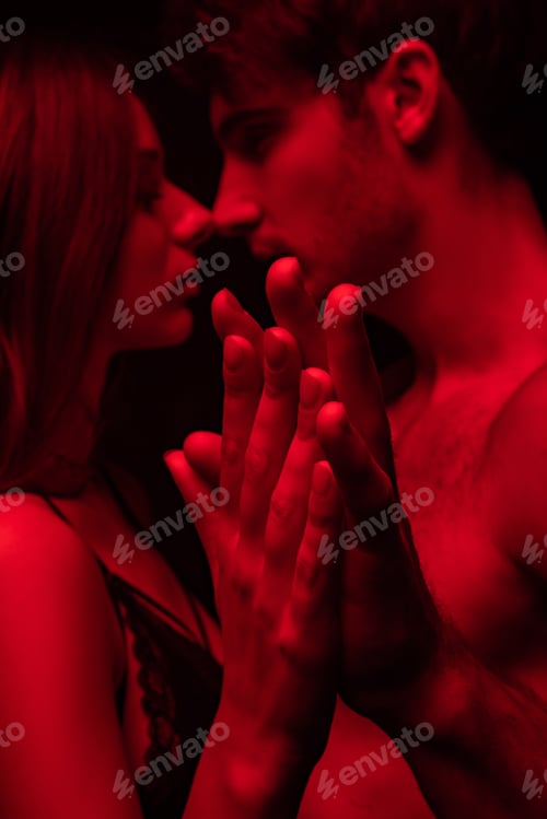 Preview: side view of passionate undressed sexy young couple kissing and holding hands in red light isolated