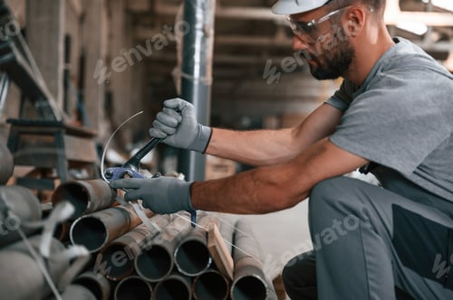 Preview: Sitting and working. Young man at the factory in grey uniform