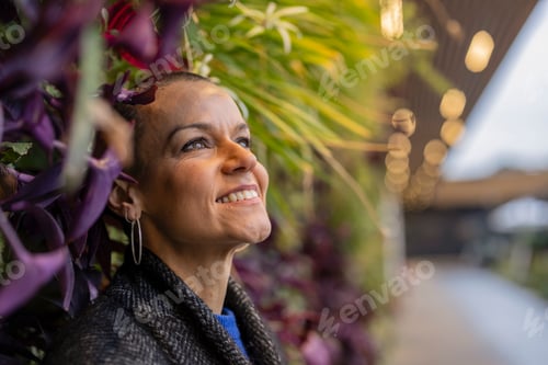 Preview: Smiling businesswoman looking up near colorful plants in modern office building