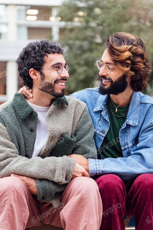 Preview: couple of gay men sitting in a park smiling happy