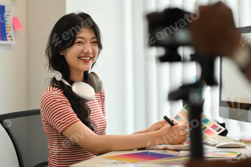 Preview: Cheerful female freelancer working on new design project and recording vlog on digital camera