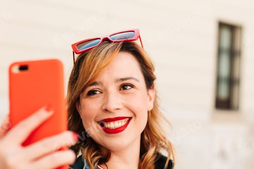 Preview: Beautiful young woman taking a selfie with her smartphone on the street of her city. Lifestyle.