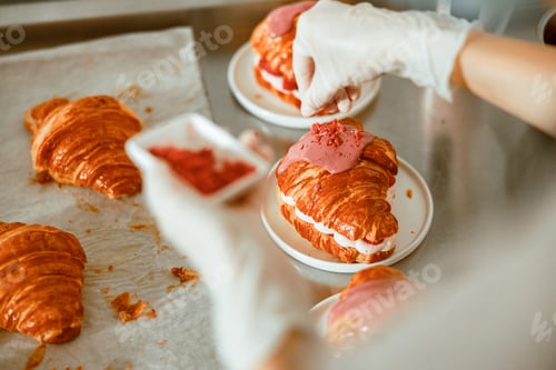 Preview: Lady scatters pink sprinklings onto delicious croissants on metal table