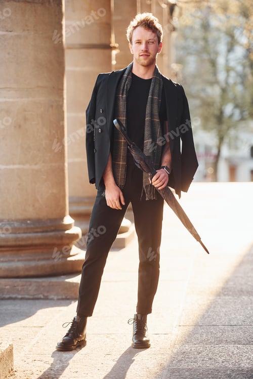 Preview: Holding umbrella. Elegant young man in formal classy clothes outdoors in the city
