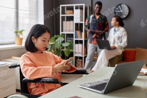 Preview: Young Asian woman with disability using smartphone working in office