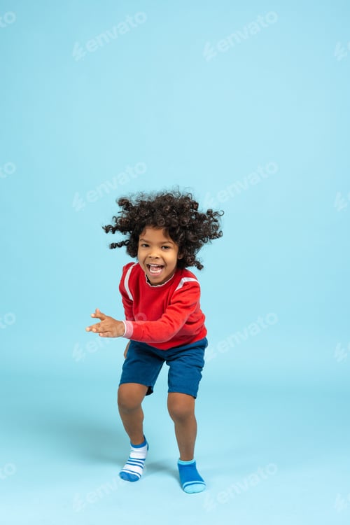 Preview: Ecstatic mixed race child with curly hair jumping, expressing joy on blue background