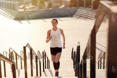 Preview: Sporty young woman running upstairs on sunny day