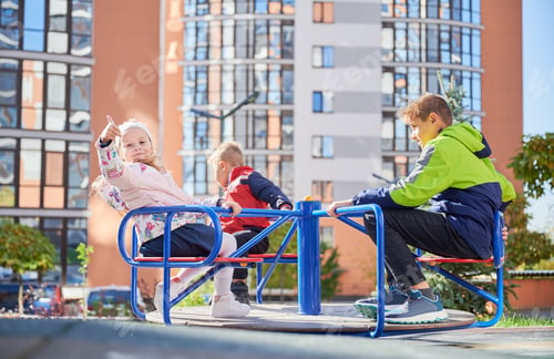 Preview: Three little kids playing on merry-go-round outdoors in spring.