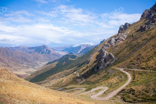 Preview: Winding serpentine dirt road on a steep mountain slope with green grass