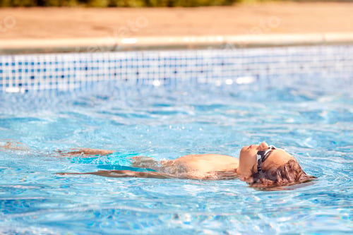 Preview: Boy Wearing Goggles Floating On Back In Swimming Pool On Summer Vacation