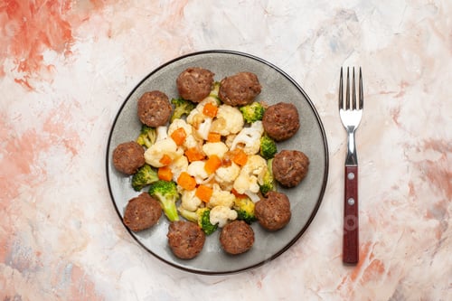 Preview: top view broccoli and cauliflower salad and meatball on plate a fork on nude isolated background