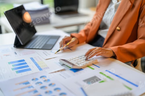 Preview: Businesswoman analyzing financial charts and using calculator in office