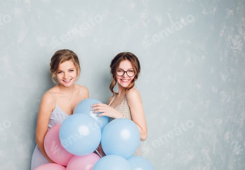 Preview: Two girls having fun in a studio and playing with blue and pink balloons. Blond girl wears blue