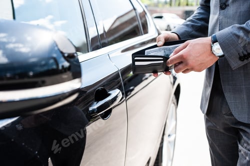 Preview: cropped shot of businessman counting money in wallet at car on street