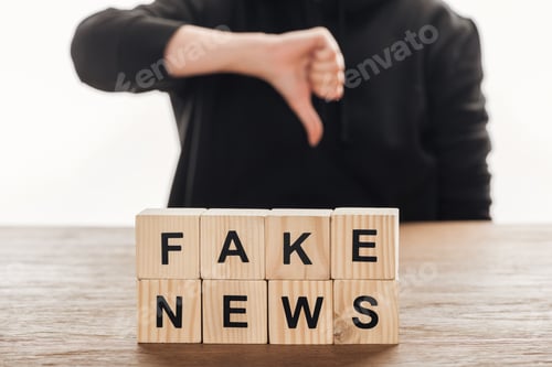 Preview: cropped image of journalist showing thumb down to wooden cubes with words fake news at wooden table